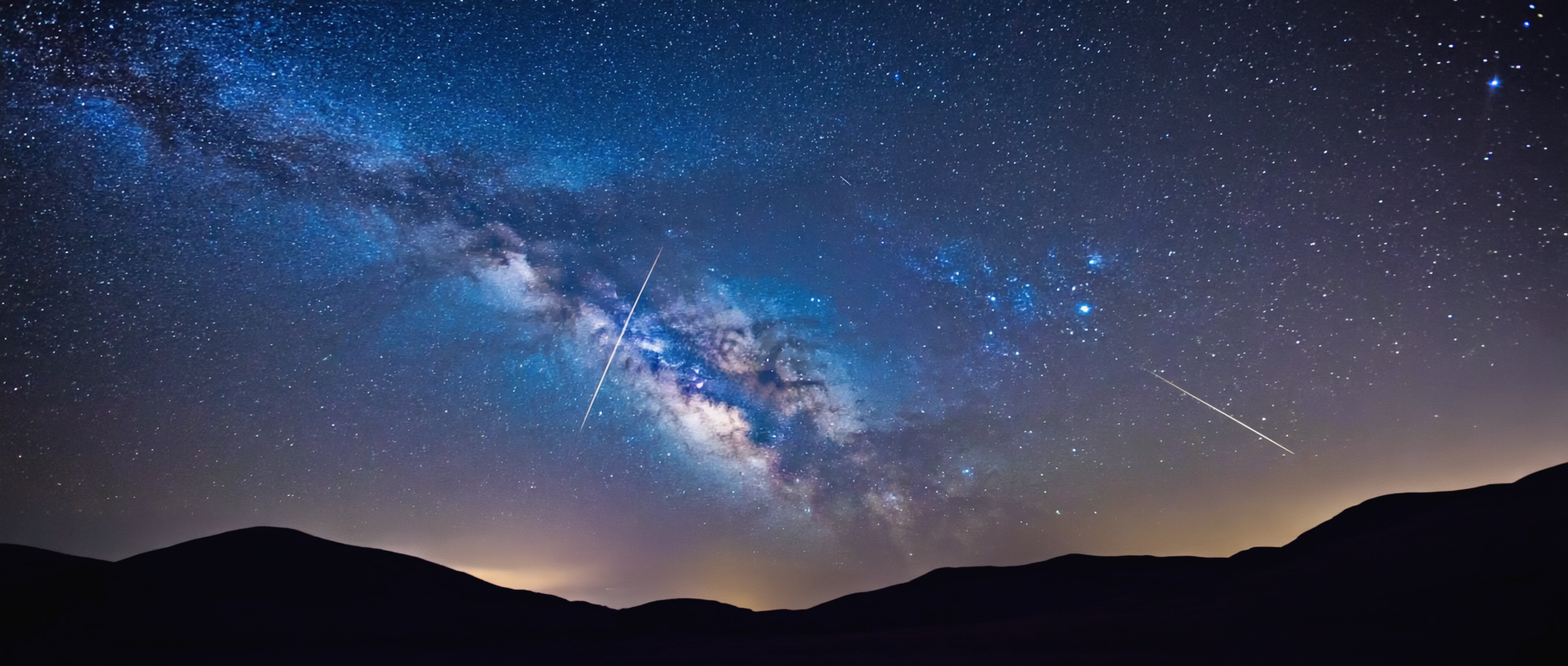 Nachthimmel mit Meteor-Spur und Milchstrasse über einer dunklen Landschaft